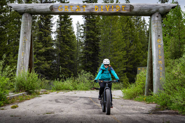 Cyclist passes old Great Divide display where North American tributaries split in the Rocky Mountains . Banff National Park Alberta, June 24 2024: Cyclist passes under the old Great Divide display where North American tributaries split in the Rocky Mountains Continental Divide. Great Divide Mountain Bike Route stock pictures, royalty-free photos & images