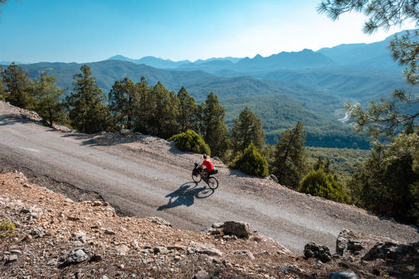 Mountain range in background with bike with bag going uphill.The shadow of the bike is big Morning hours below the ramp road cyclist in motion background valley and mountain range blue light sky bikepacking stock pictures, royalty-free photos & images